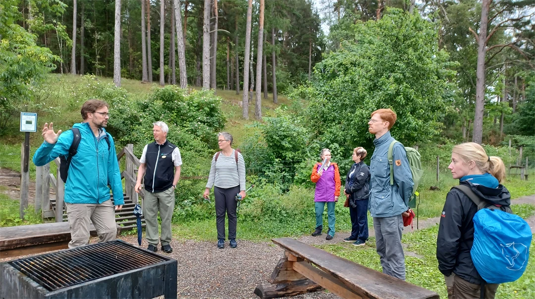 En grupp människor står och pratar vid en eldplats i stadsnära landskap