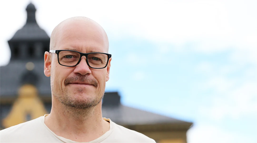 Glasögonprydd man med tak och himmel i bakgrunden.