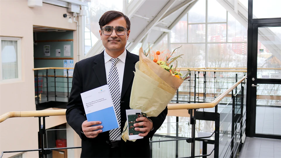 A man in a suit holds a thesis and a bouquet of flowers
