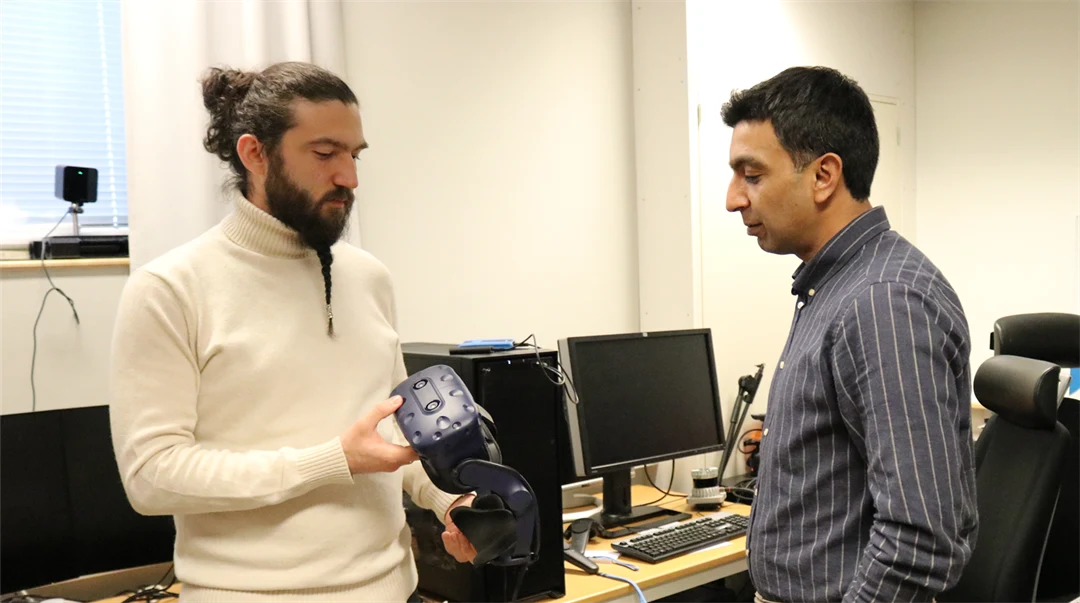 Två män står tillsammans i en datasal. Den ena mannen håller i ett par VR-glasögon.