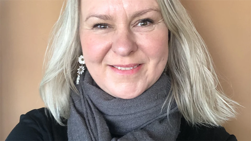 Ett porträttfoto av en blond kvinna mot en ljusbeige bakgrund