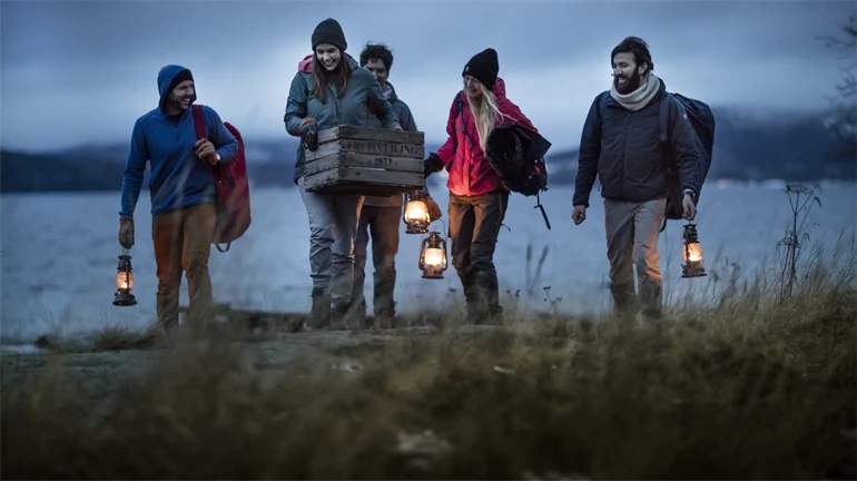 Fem personer går med lyktor vid stranden i skymning på Höga Kusten