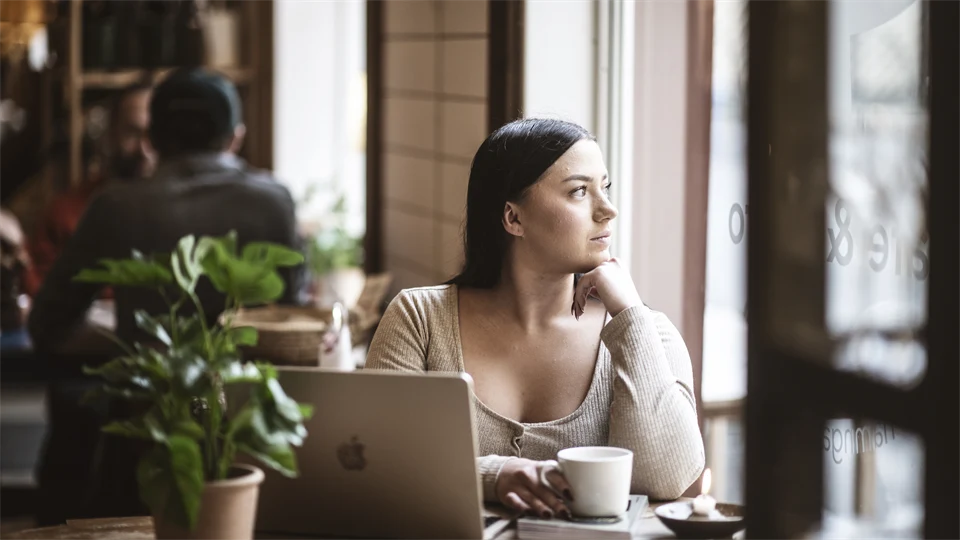 A woman is sitting at a table, looking out of a window.