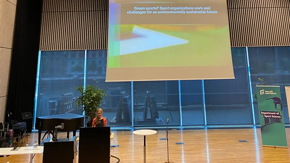 Forskaren Susanna Hedenborg står framför en talarstol i en stor konferenslokal 