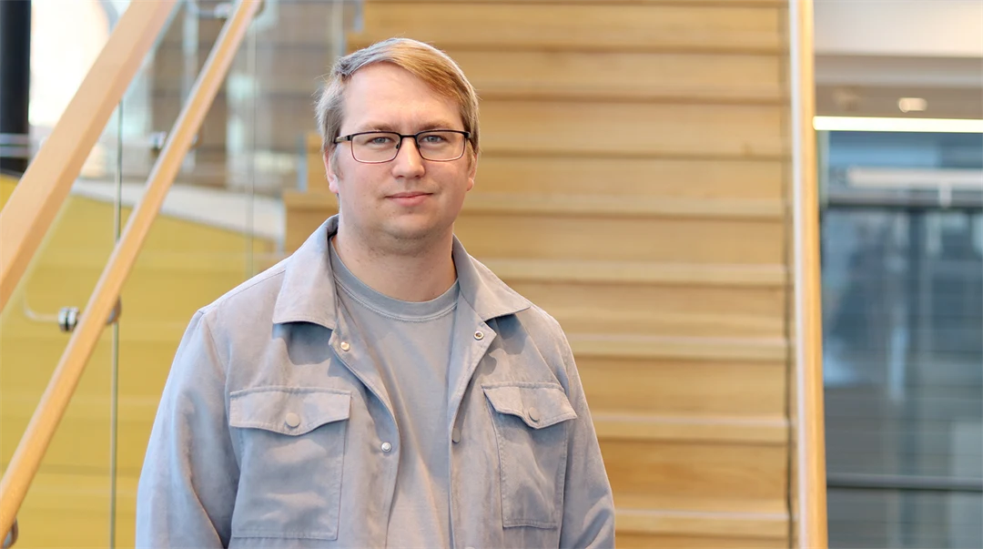 A man with glasses stands in front of a staircase.