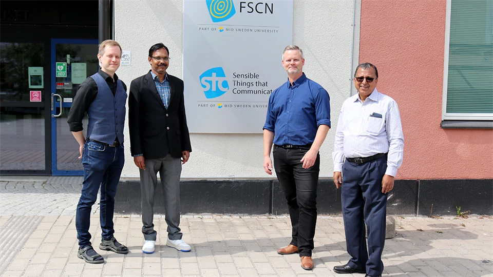 Four men standing at a facade sign with the text STC Research Center.