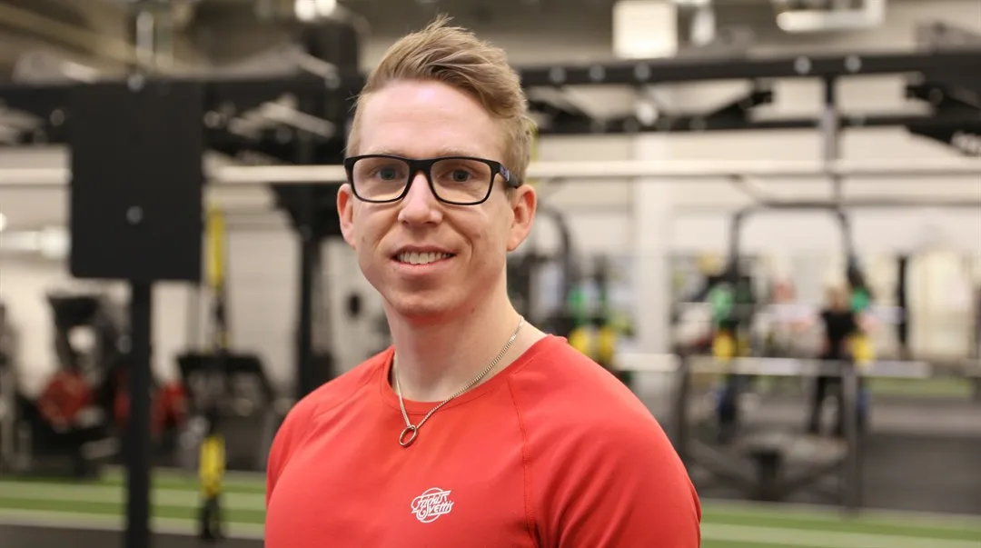 Robin Andersson Nyberg porträtterad på sitt jobb på Friskis & Svettis, i bakgrunden syns träningsredaskap.