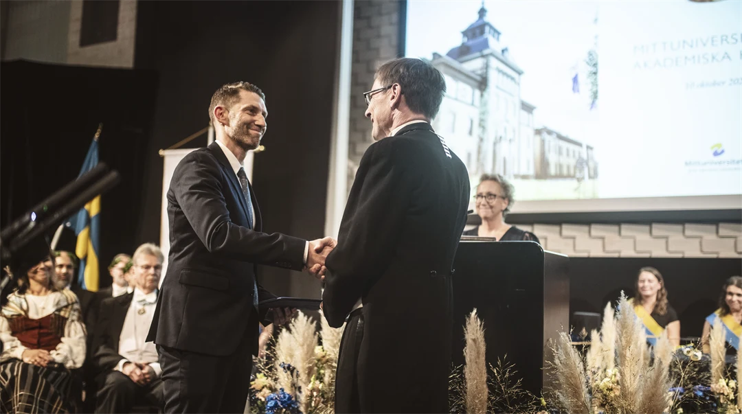 Två finklädda män skakar han på en scen. 