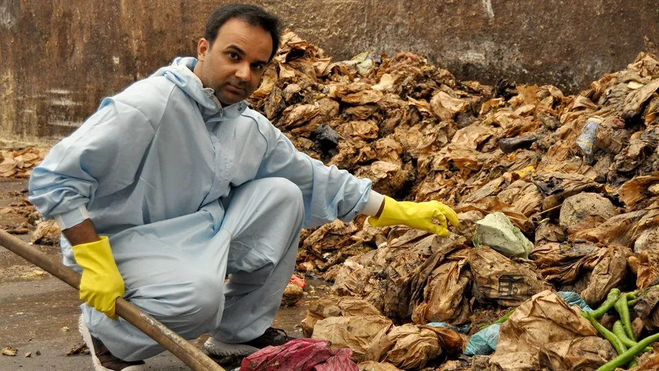 Person dressed in a blue coverall looking through old garbage bags.