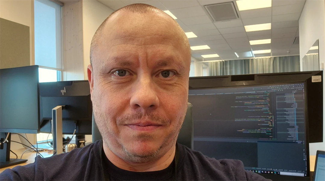 En man sitter i ett kontorslandskap med en datorskärm bakom sig.