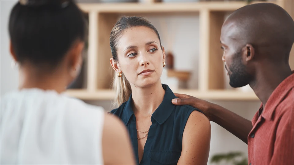 Tre personer i ett rum där två stöttar den tredje genom samtal.