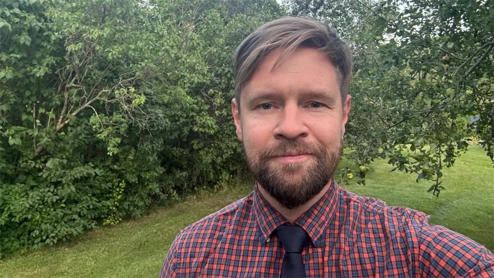 En man med brunt hår, skägg och en röd svart skjorta