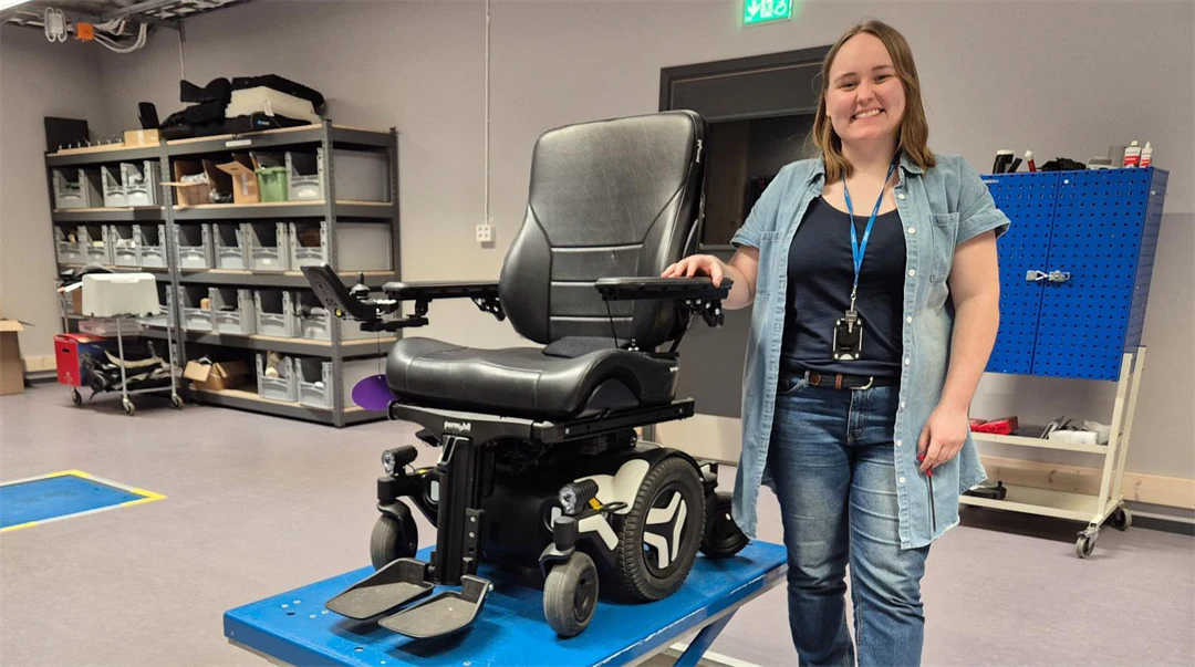 En kvinna står bredvid el elektrisk rullstol som är upphissad.