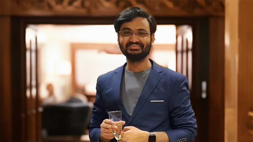 A man looks into the camera and smiles. He is holding a glass in his hand.