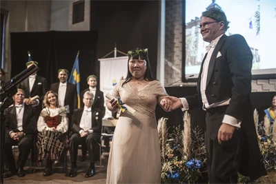 Två finklädda personer med lagerkransar står på en scen.