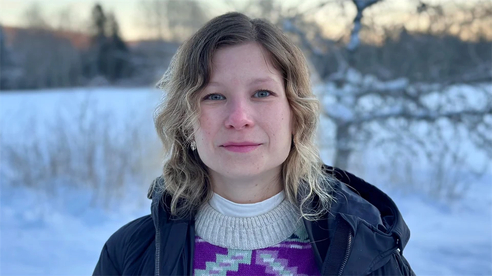 Kvinna med axellångt hår och jacka i förgrunden och ett vinterlandskap i bakgrunden