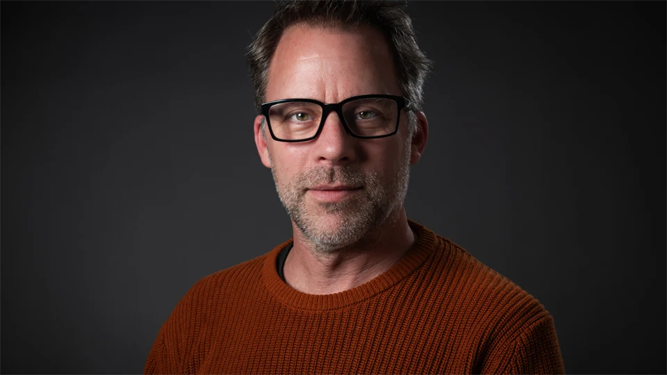 Man in dark glasses and dark red knitted sweater poses in front of the camera.