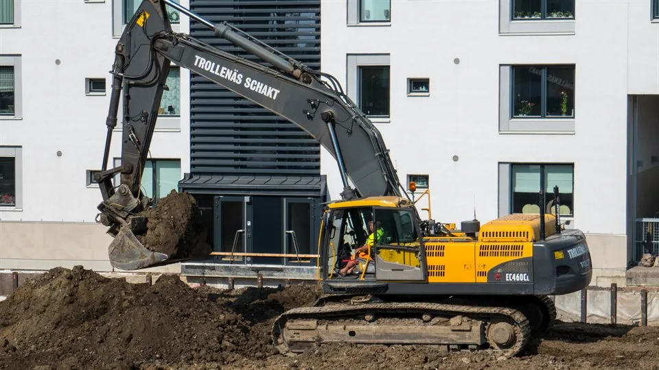 Yellow excavator digging in front of a white apartment house