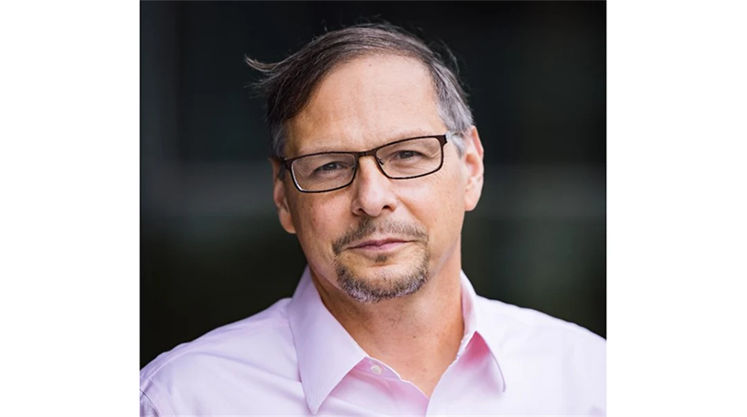 A dark-haired man in glasses, wearing a pink shirt.