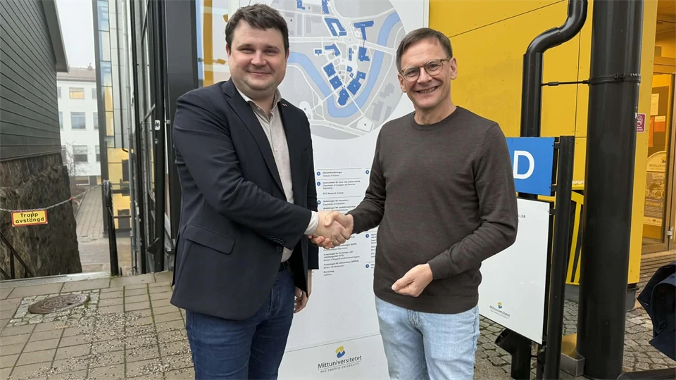 Två män står utomhus och skakar hand med varandra. 