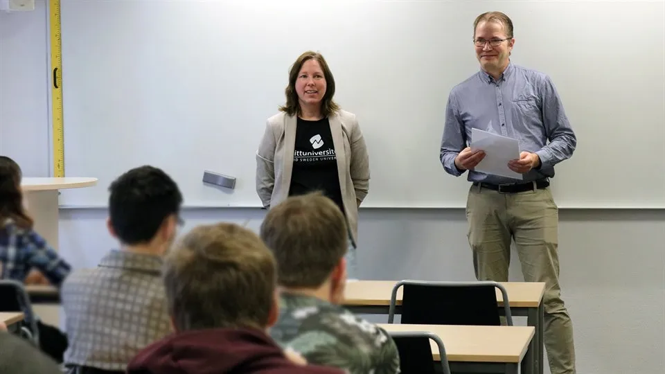En kvinna och en man som presenterar för en skolklass i en lektionssal.