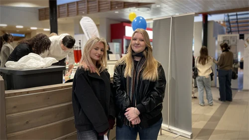 Två personer, båda med ljust hår och mörka kläder, ler och tittar in i kameran.