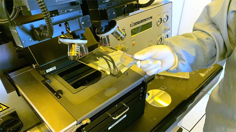 Hand holding a square plate under a microscope.