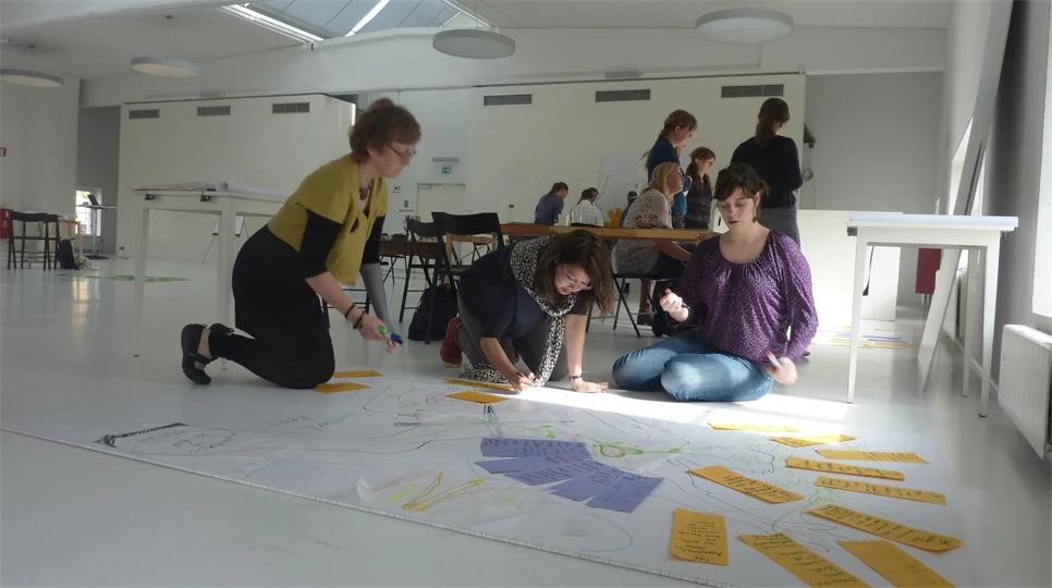 Tre personer sitter på golvet och klipper och klistrar under workshop