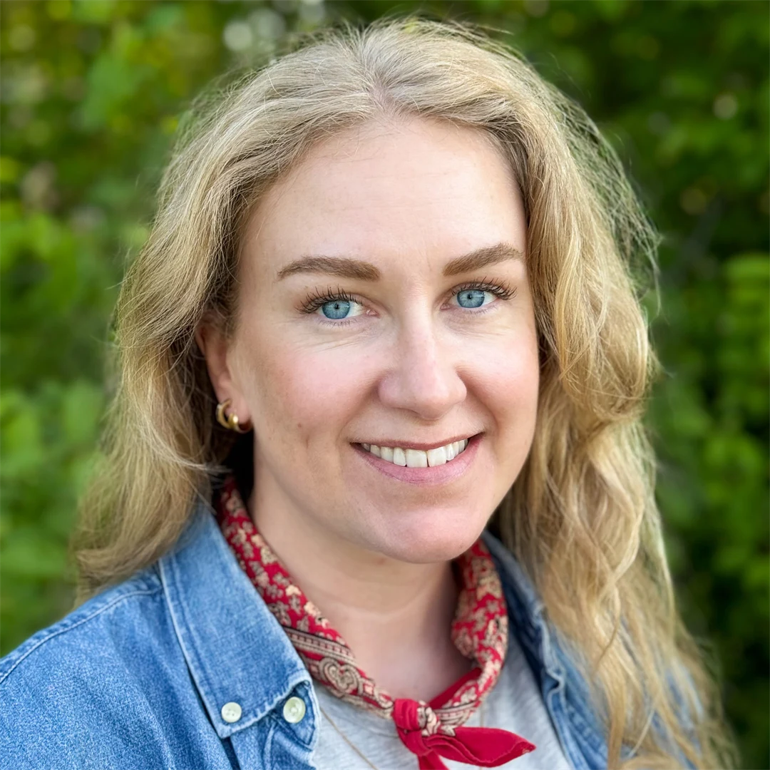 En kvinna med långt, ljust hår, klädd i jeansskjorta, tittar in i kameran.