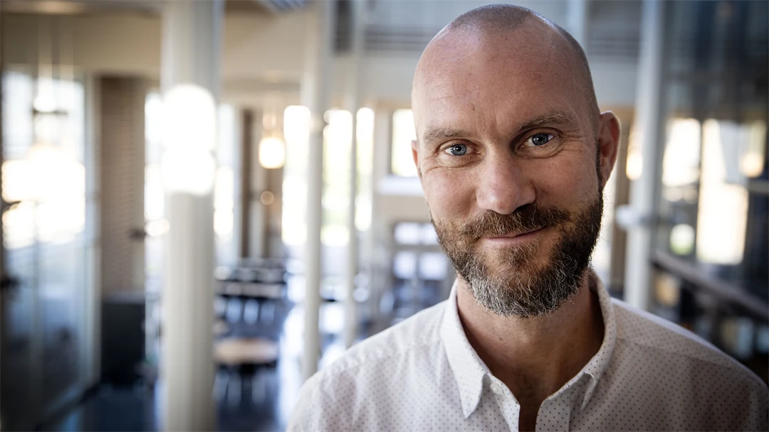 Man med skägg och vit skjorta står i en stor hall.