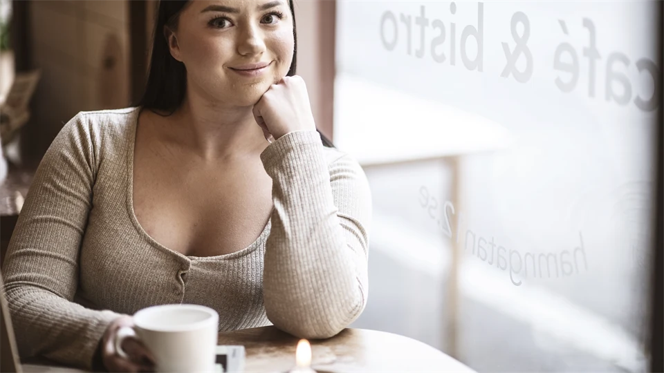 En kvinna sitter vid ett fönster. Hon tittar leende mot kameran.