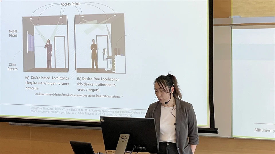 En kvinna med mörkt hår uppsatt i en hästsvans står vid en dator och håller en presentation.