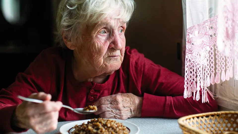 Äldre dam som äter och tittar genom fönster