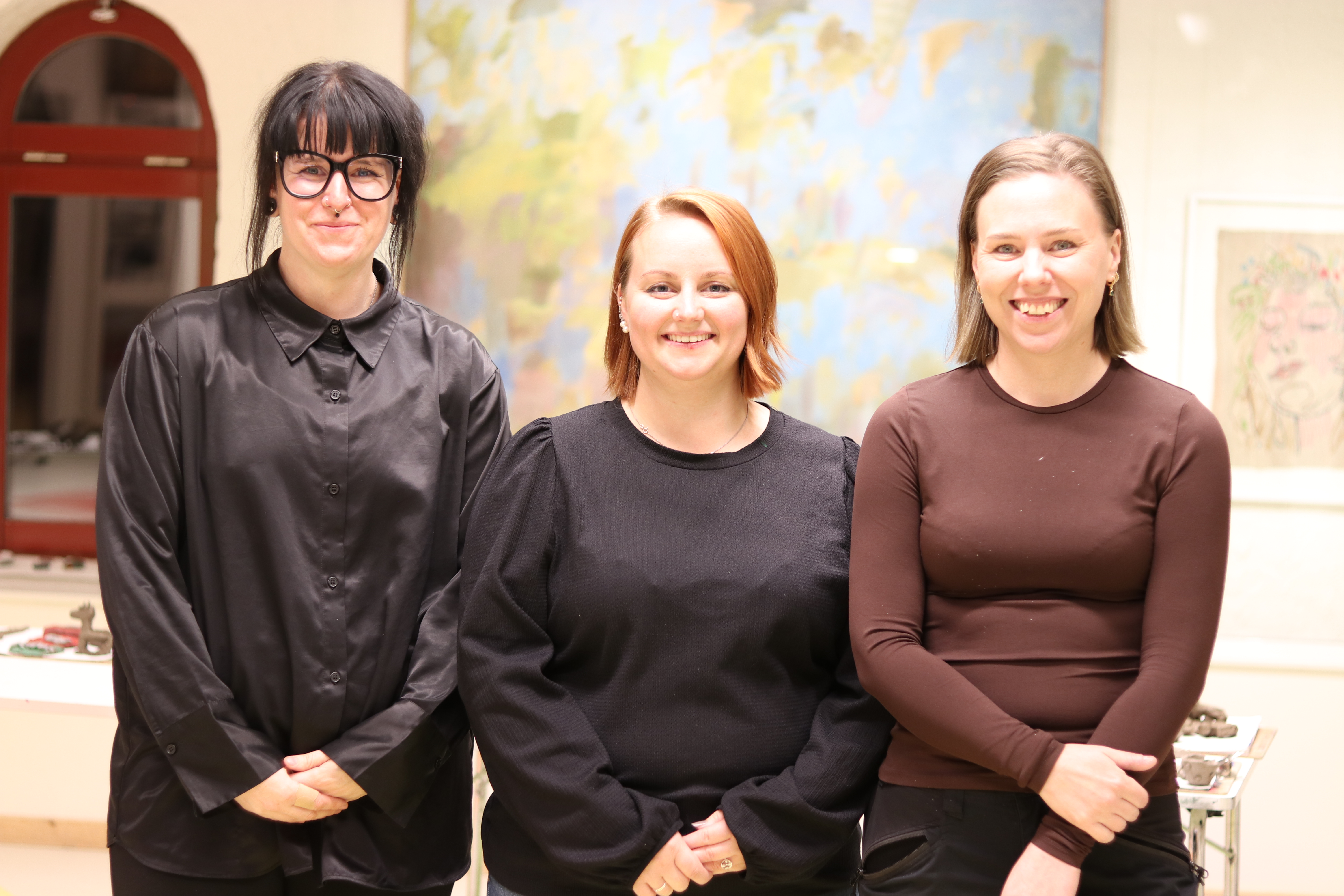 Tre kvinnor står i en klassrumsmiljö med en världskarta i bakgrunden. 