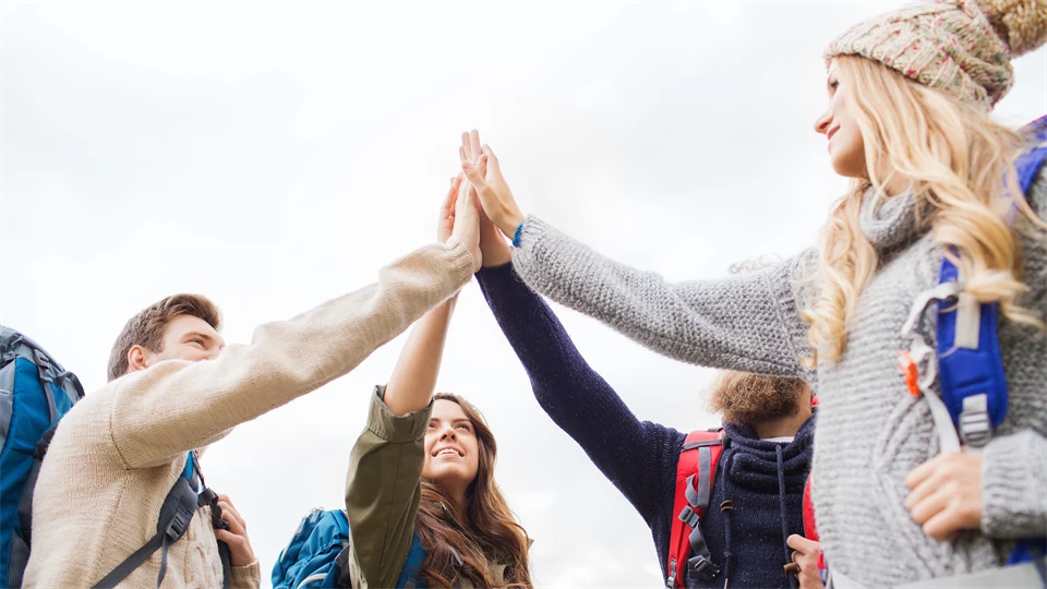 En grupp människor med ryggsäckar på sig står i en ring och gör en high five