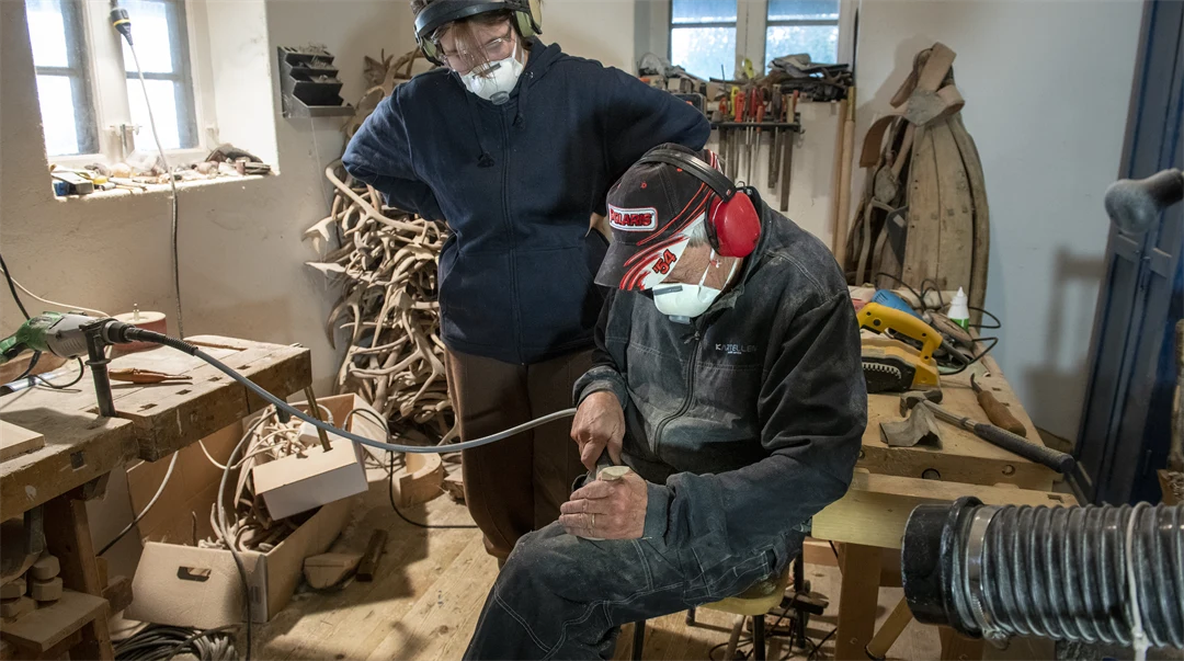 En man visar en ung person hur man slöjdar en kåsa