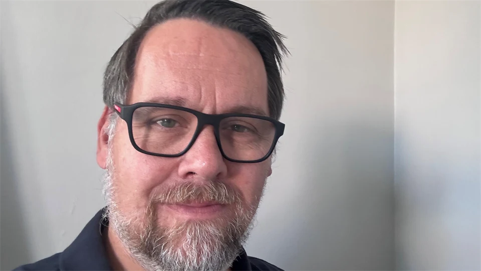 Porträttfoto av en man med brunt hår och mörka glasögon