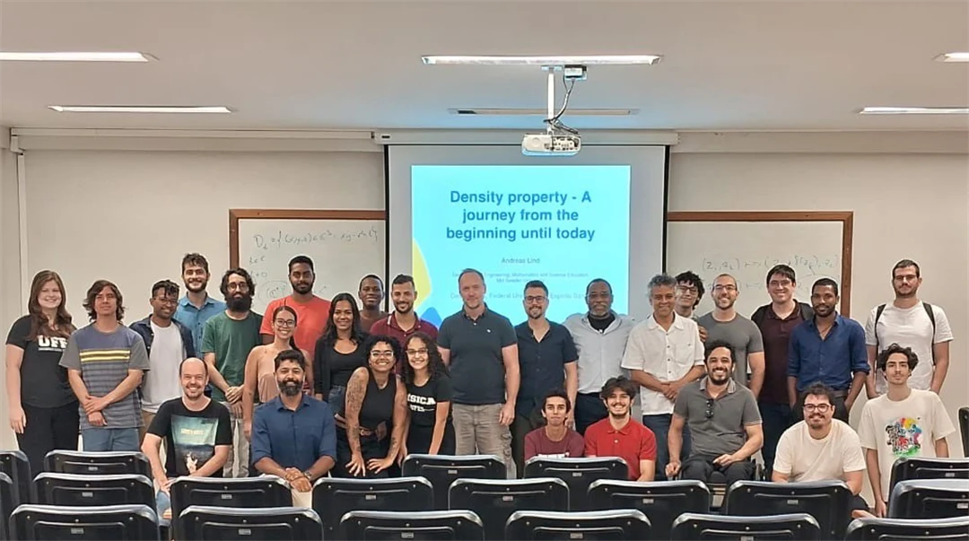 A group of people stand together in front of a monitor in a lecture hall.