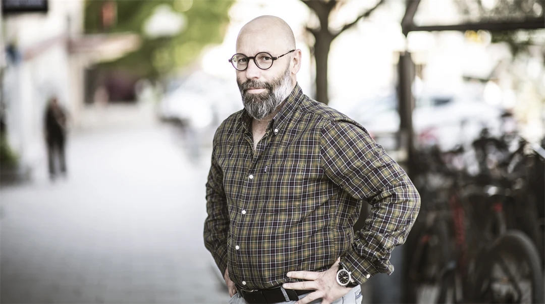 Man med rutig skjorta ler mot kameran