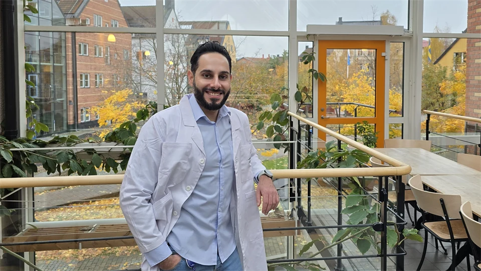 A man wearing a white lab coat stands in a lighted courtyard.