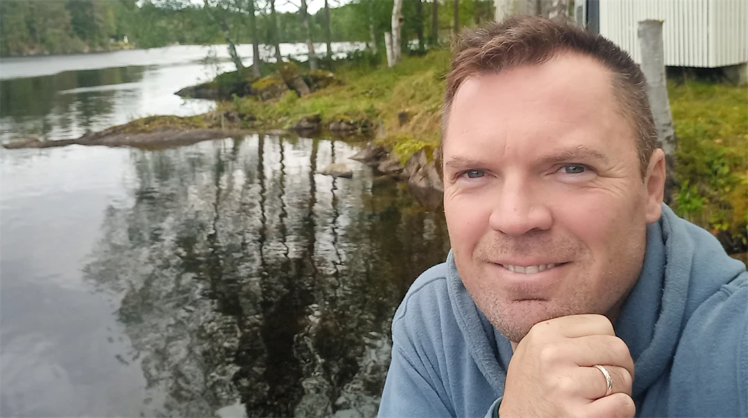 En man sitter vid ett vattendrag, lutar hakan mot handen