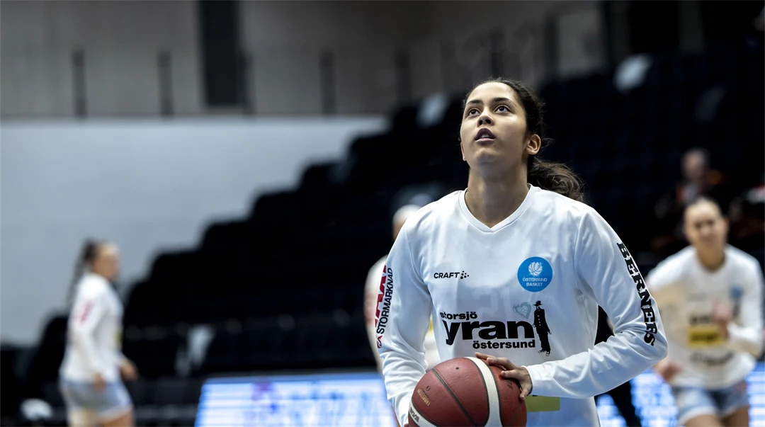 Ung kvinna ska till att skjuta en basketboll mot korgen.