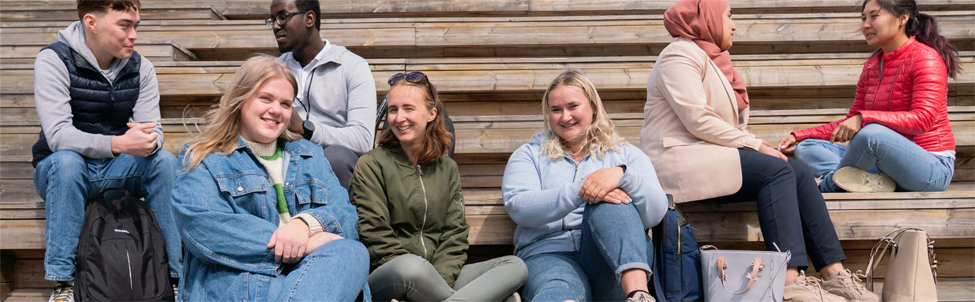 En grupp studenter sitter i en trätrappa och pratar.