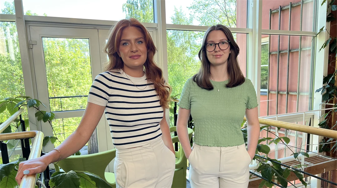 Två unga kvinnor står tillsammans i en ljusgård.