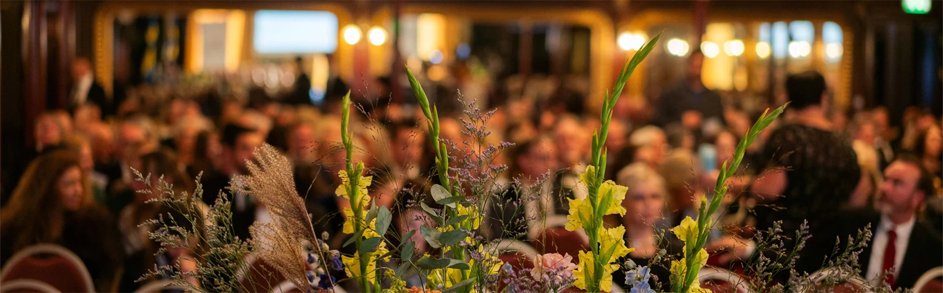 Blomsterarrangemang på en scen med uppradade stolar i bakgrunden.