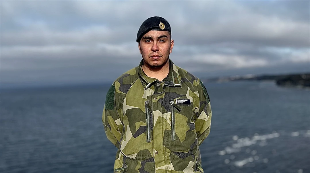 En man i militärkläder står på en klippa med havet i bakgrunden