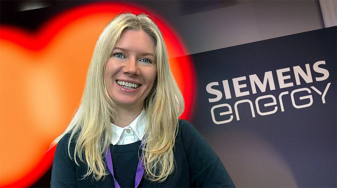 En kvinna med ljust hår ler, i bakgrunden en företagslogga.