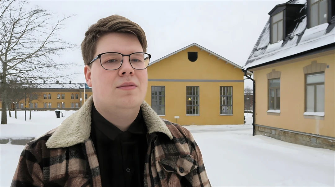 Manlig student står på campusgården i Östersund framför några av byggnaderna. Gården är snötäckt och studenten har vinterjacka på sig.