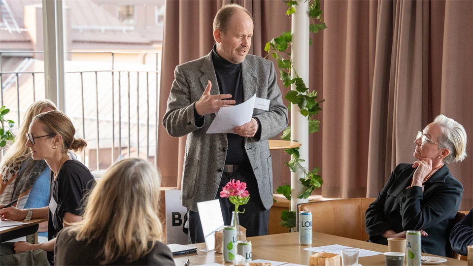 Personer runt ett bord som lyssnar till en manlig talare