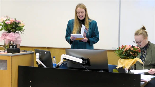 Ung kvinna läser ur avhandling i en lektionssal